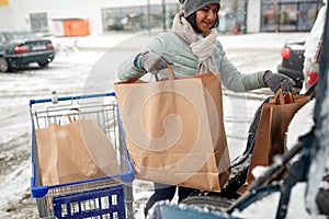 Woman loading food from shopping cart to car trunk