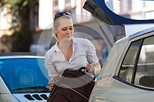 Woman loads suitcase into car boot or trunk