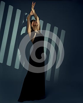 Woman in long Black Dress perform on Art Stage. Elegant Lady in evening Gown over striped spotlight Background. Beautiful dancing