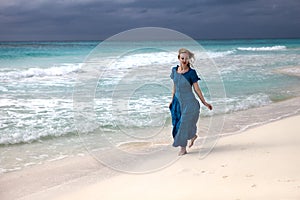 Una mujer en largo tiempo azul ropa va sobre el bullicioso el mar Costa 