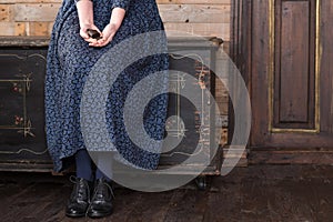 A woman in a long blue dress is sitting on a black chest and holding an old lock with a key