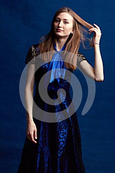 A woman with long brown hair, in a blue dress, studio portrait on a blue background