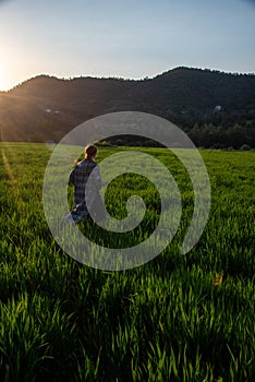 Woman with long coat holding long hair enjoying sunset on the green meadow