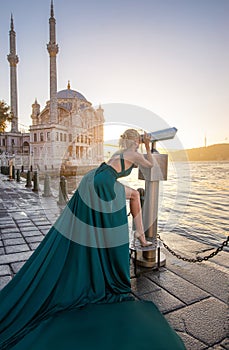 Woman in long green dress posing at the historical square near OrtakÃ¶y mosque and Bosphorus waters