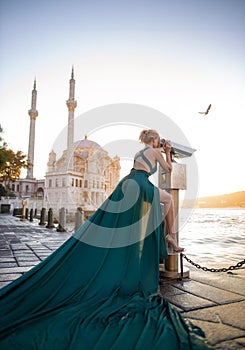 Woman in long green dress posing at the historical square near OrtakÃ¶y mosque and Bosphorus waters