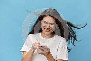 woman with long hair blowing in the wind, in a T-shirt, holding a fashionable smartphone in her hands and aggressively
