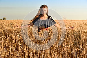 A woman with long hair in a dress of peas stands among the wheat flocks in the field