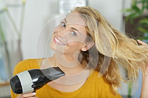 woman with long hair dries hair with hairdryer