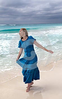 Woman with long hair fluttering in the wind in a blue dress on the shore of a stormy sea on a sandy beach Cuba, Varadero