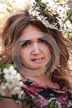 Woman with long hair looking at camera near blooming cherry branches in garden