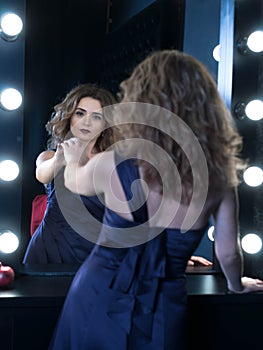 woman with long hair in purple draped dress touching reflaction in mirror with hand