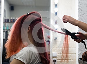 Woman with long hair sitting on the Curling procedure curls using Curling irons in the salon hairdresser