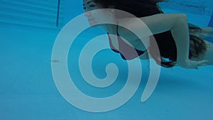 Woman with long hair swims underwater in pool.