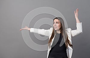 Woman with long hair in a white jacket waves her hands and is surprised at the gray background, emotions