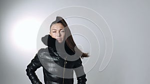 Woman with long hair in wind in down jacket posing in studio on white background