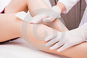 Woman with long perfect legs and smooth skin having wax stripe depilation hair removal procedure on legs in beauty salon