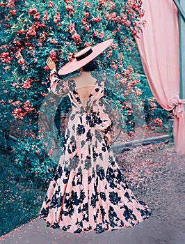 A woman in a long pink dress and a hat stands with her back to the camera
