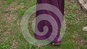 The woman in the long purple dress walks on the grass