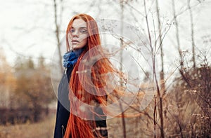 Woman with long red hair walks in autumn on the street. Mysterious dreamy look and the image of the girl. Redhead woman walking