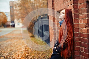 Woman with long red hair walks in autumn on the street. Mysterious dreamy look and the image of the girl. Redhead woman walking