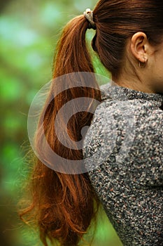 woman with long thick brown hair pony tale close up photo on green summer garden background