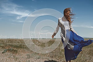 Woman with long tousled hair next to the wind turbine with the wind blowing