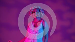 Woman in look of Marilyn Monroe in studio in pink and green neon light on pink background with highlights. Woman