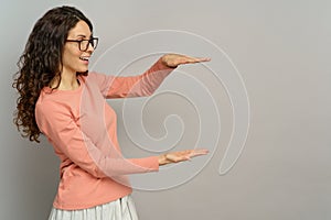 Woman look at something in hand hold open palm for presentation over copyspace at gray background