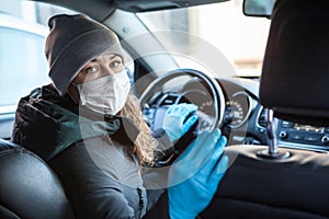 Woman looking back while sitting on driver seat inside car in facemask and blue gloves, personal hygiene