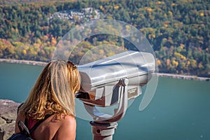 Woman looking through binoculars at scenic overlook in autumn