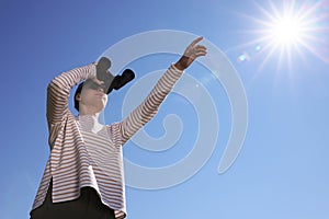 Woman looking through binoculars outdoors on sunny day, low angle view