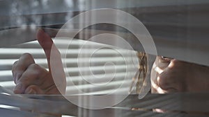 Woman looking through the blinds of the window to the street