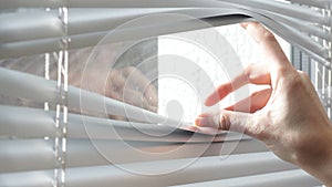 Woman looking through the blinds of the window to the street