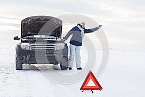 Woman looking on the broken car looking at the motor. Around winter and snow field.