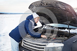 Woman looking on the broken car looking at the motor. Around winter and snow field.