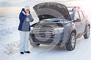 Woman looking on the broken car looking at the motor. Around winter and snow field.