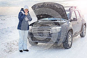 Woman looking on the broken car looking at the motor. Around winter and snow field.