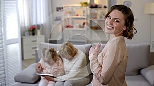 Woman looking at camera, daughter and granny playing tablet, togetherness