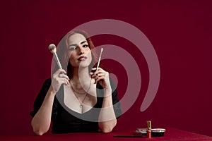 Woman looking at camera while holding makeup brushes standing against an  background.