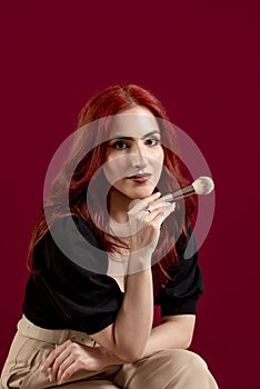 Woman looking at camera while holding makeup brushes standing against an  background.