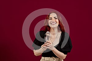 Woman looking at camera while holding makeup brushes standing against an isolated background.