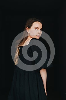 Woman looking at the camera over her shoulder. In black dress over black