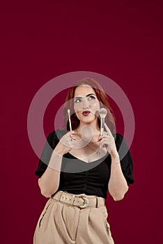 Woman looking at camera while holding makeup brushes standing against an  background.