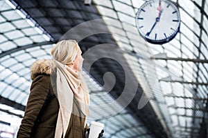 Woman looking at clock in train station as her train has a delay photo