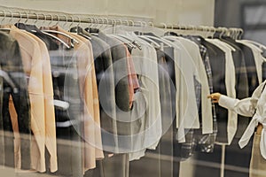Woman is looking at clothes in a store. Clothes are hanging on racks. Blurred view through store window