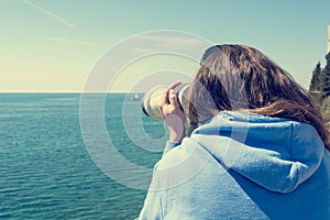 Woman looking through coin operated binoculars at seaside.
