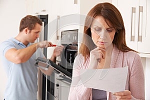 Woman Looking Concerned At Bill For Repair Of Kitchen Appliance