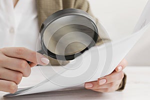 Woman looking at document through magnifier at table, closeup. Searching concept