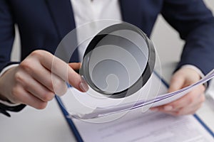 Woman looking at document through magnifier at table, closeup. Searching concept