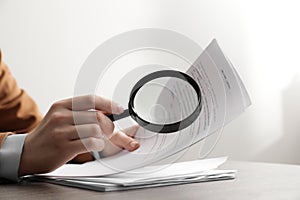 Woman looking at document through magnifier at table, closeup. Searching concept
